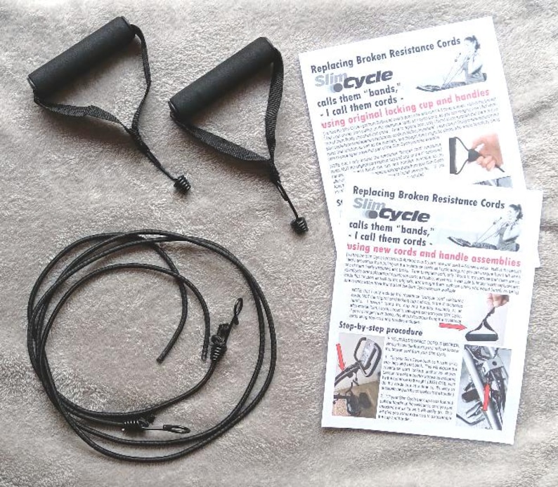May include: A set of black exercise equipment replacement parts, including two handles, a long cord, and two instruction sheets. The text on the sheets reads "Replacing Broken Resistance Cords" and "Slim Cycle".