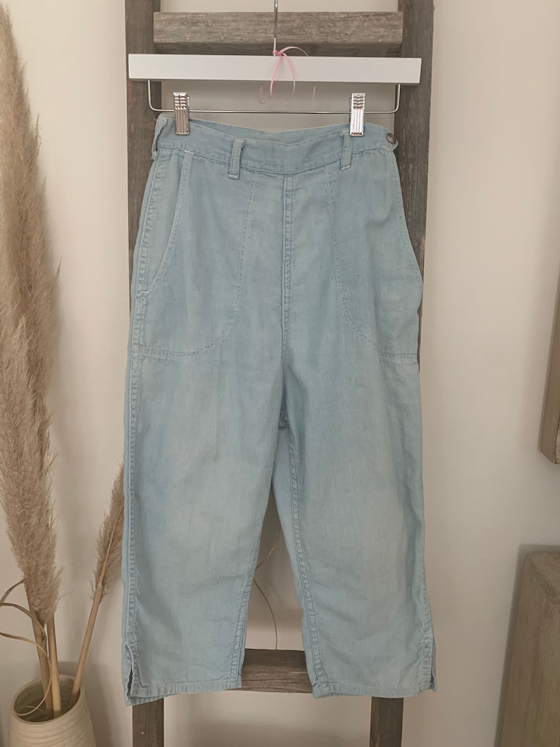May include: Light blue denim pants with a high waist and two large pockets on the front. The pants are cropped and have a relaxed fit.