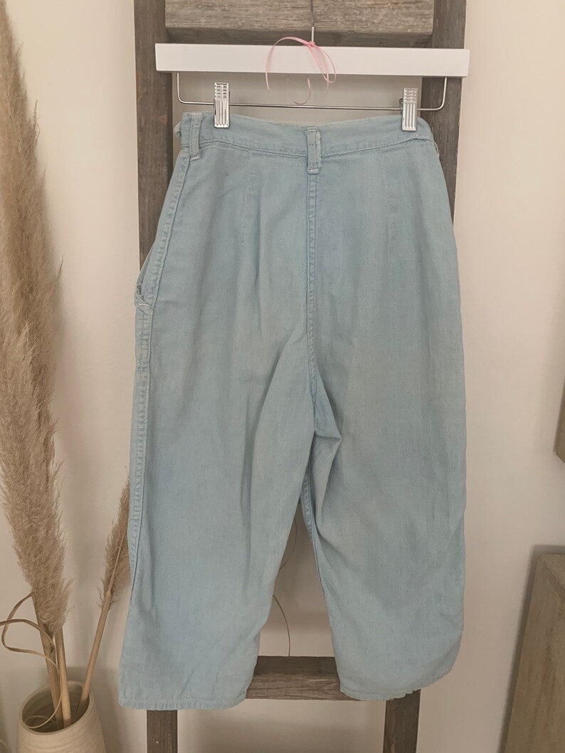 May include: Light blue denim pants with a high waist and a straight leg. The pants have a button fly and belt loops.