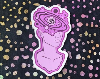 May include: A pink sticker with a line drawing of a head with a galaxy and the symbol Om inside it.