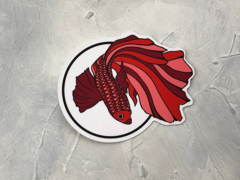 May include: A red and pink betta fish sticker with a white background and a black circle border.