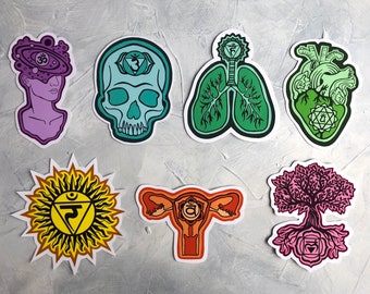 May include: Seven colorful stickers with illustrations of the seven chakras. Each sticker features a different symbol and color representing a chakra. The stickers are on a gray background.