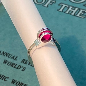 Puede incluir: Un anillo de plata con una piedra preciosa rosa engastada en un diseño geométrico.