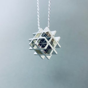 May include: A silver geometric pendant necklace with a cube-shaped design. The pendant is made of interconnected squares and has a modern, minimalist aesthetic.