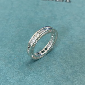 May include: A silver ring with a double band design. The outer band has a row of small, round, white stones.
