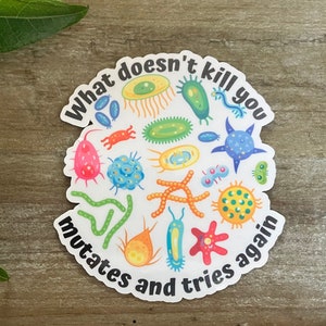 May include: A white sticker with a black circle and the text "What doesn't kill you mutates and tries again." Inside the circle are colorful cartoon illustrations of various microbes.