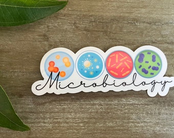 May include: A white sticker featuring four colourful petri dishes containing various types of bacteria. The text "Microbiology" is written in cursive beneath the dishes.