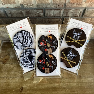May include: Three sets of car coasters with different designs. The first set features a fingerprint design, the second set features a crime scene design with blood splatter, and the third set features a skull with caution tape.