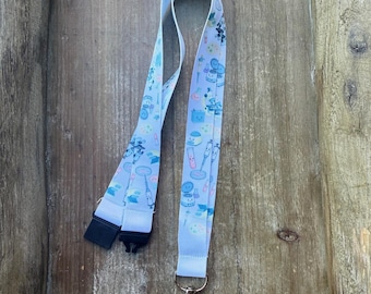 May include: A light blue fabric lanyard featuring a repeating pattern of colorful cartoon laboratory equipment, including beakers, test tubes, and syringes. The lanyard includes a black plastic breakaway clasp and a silver metal swivel hook.