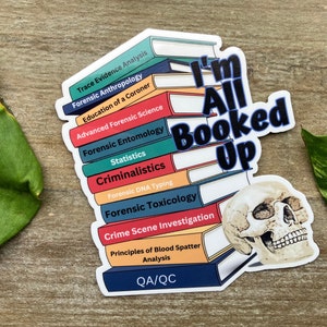 May include: A sticker with a stack of books and a skull. The books have titles related to forensic science, such as "Trace Evidence Analysis", "Forensic Anthropology", and "Forensic Toxicology". The text "I'm All Booked Up" is written across the books.