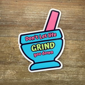 May include: A sticker featuring a blue mortar and pestle design with the text "Don't Let life GRIND you down" in a playful font. The text is in a mix of colors, including pink, blue, and yellow. The sticker has a white border.