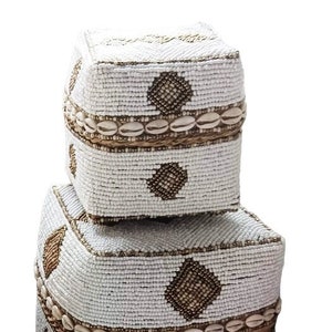 May include: Three white beaded boxes with brown diamond patterns and a brown shell trim. The boxes are stacked on top of each other.