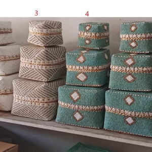 May include: Five stacks of decorative boxes with intricate woven patterns. The boxes are made of natural materials and feature a variety of colors, including white, beige, blue, and black.