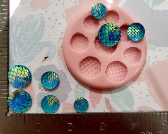 Könnte beinhalten: Eine Silikonform mit sechs runden Vertiefungen, jede mit einem strukturierten Design, das an Fischschuppen erinnert. Es gibt acht regenbogenfarbene runde Harzstücke in Blau und Grün, von denen sich einige in der Form befinden.