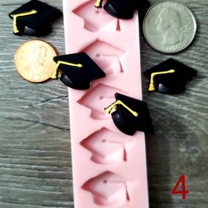 Könnte beinhalten: Eine rosa Silikonform mit sechs Abdrücken von Abschlusskappen, neben mehreren schwarzen Abschlusskappen mit gelben Quasten. Ein Cent und ein Vierteldollar sind ebenfalls vorhanden, zusammen mit der roten Zahl 4.