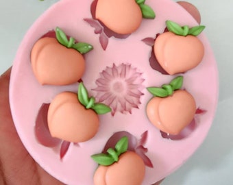 May include: A pink silicone mold with six peach-shaped cavities. Each cavity has a small green leaf detail.