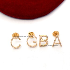 Peut inclure: Trois boucles d'oreilles initiales en or avec des pierres en zircone cubique transparentes. Les lettres sont C, G et A.