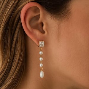 May include: Gold-toned drop earrings featuring a square, clear gemstone at the top, followed by a series of small, round pearls and a larger, teardrop-shaped pearl at the bottom. The earrings are a classic and elegant accessory.