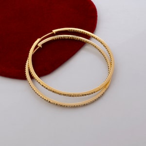 May include: Gold hoop earrings with a row of small clear stones around the edge. The earrings are on a red background. "Seventy Seven Jewelry" is written on the earrings.