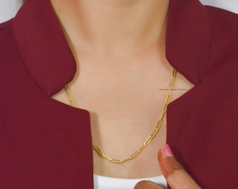 May include: A gold chain necklace with a paperclip link style. The necklace is worn by a person with a maroon blazer.