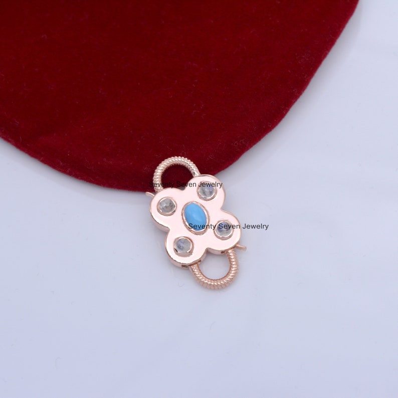 Op de afbeelding: Roze gouden metalen sluiting met een turquoise en wit edelsteen ontwerp. De sluiting is gevormd als een bloem met vier bloemblaadjes.  Seventy Seven Jewelry is op de sluiting gedrukt.