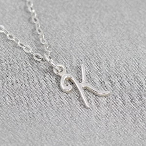 May include: A silver chain necklace with a delicate cursive letter K pendant.