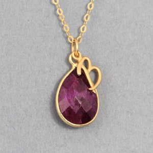 May include: A gold necklace with a teardrop-shaped purple gemstone pendant and a gold letter 'B' charm.