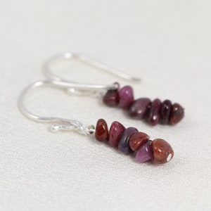 May include: A pair of silver dangle earrings with a cluster of red and purple gemstone chips.