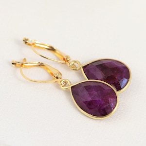 May include: A pair of gold earrings with teardrop-shaped purple gemstones.