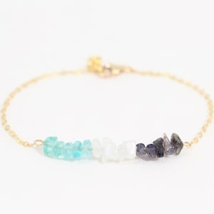 May include: A gold chain bracelet with a graduated row of light blue, white, and dark blue gemstone chips.