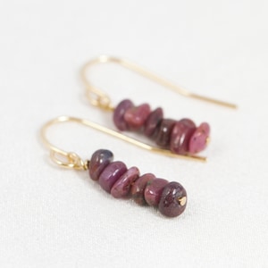 May include: A pair of gold earrings with a cascade of pink and red gemstone chips. The earrings are made with a simple gold hook.