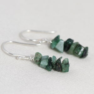 May include: A pair of silver dangle earrings with a cluster of green emerald chips.