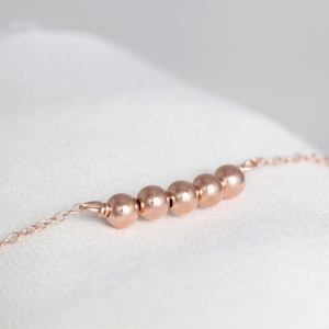 May include: A delicate rose gold chain bracelet with five round beads.