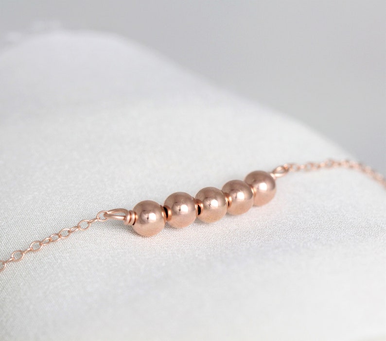 May include: A delicate rose gold chain bracelet with five round beads.
