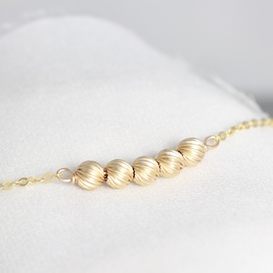May include: A gold chain necklace with a row of five gold beads. The beads have a textured, ribbed surface.