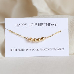 May include: A gold necklace with four beads and a card that says "Happy 40th Birthday! Four beads for four amazing decades!"