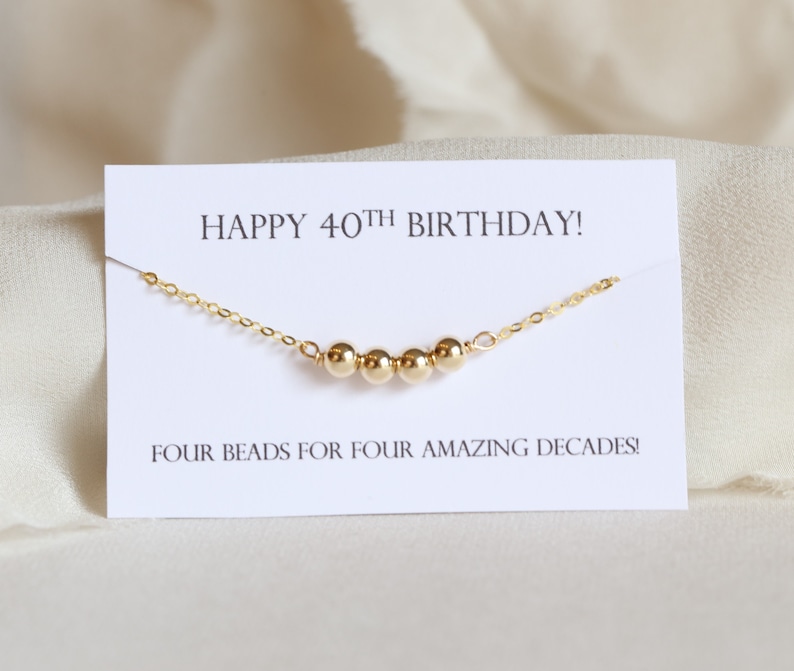 May include: A gold necklace with four beads and a card that says "Happy 40th Birthday! Four beads for four amazing decades!"