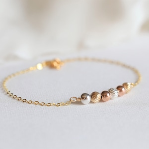 May include: A gold chain bracelet with a row of five beads in different shades of gold, silver, and rose gold.
