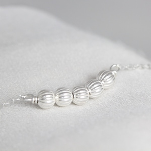May include: A silver chain necklace with a row of silver beads. The beads are round and have a textured surface.