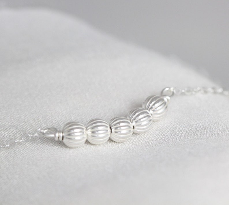 May include: A silver chain necklace with a row of silver beads. The beads are round and have a textured surface.