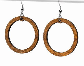 Puede incluir: Un par de pendientes circulares con un acabado de veta de madera marrón en la parte frontal y un borde negro sólido. Cada pendiente cuelga de un gancho de metal plateado, creando un diseño de aro simple con una textura de veta visible.