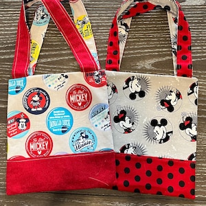 May include: Two small red and white fabric tote bags with Disney character designs. One bag features Mickey Mouse and friends with a red polka dot bottom. The other bag features Mickey Mouse and friends with a solid red bottom.