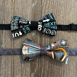 May include: Two bow ties with a black and white pattern featuring video game themed text. The top bow tie has the text "GO! NEXT LEVEL" and the bottom bow tie has the text "GAME OVER, CHECK POINT, UP, UP, UP".