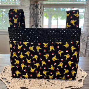 May include: Black and yellow fabric storage bin with a polka dot pattern and a Pikachu print. The bin has two handles.