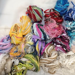 Peut inclure: Un assortiment de fils et de rubans de différentes textures et couleurs, notamment jaune, rouge, bleu, vert, rose et blanc.