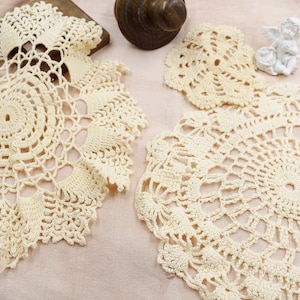 May include: Three crocheted doilies in a cream color. The doilies are circular and have a delicate lace pattern.