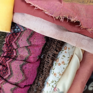 Può includere: Un mucchio di ritagli di stoffa di vari colori e motivi, tra cui rosa, marrone, bianco e crema. I tessuti sono testurizzati e alcuni hanno un motivo floreale.