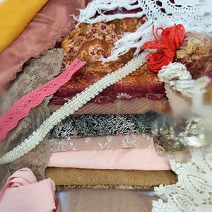 以下が含まれることがあります： さまざまな色のさまざまな生地と装飾品のコレクション。 ピンク、茶色、金、白の色合いのレース、リボン、テクスチャード加工された素材が含まれています。 赤い糸と金のスパンコールもあります。