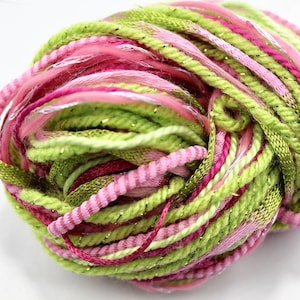 May include: A ball of colorful yarn in shades of pink, green, and white. The yarn has a textured appearance with a mix of solid and glittery strands. The yarn is suitable for knitting and other craft projects.