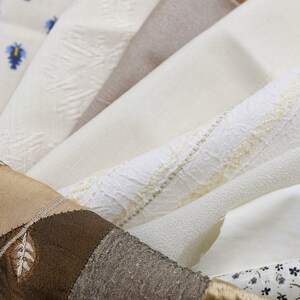 Peut inclure: Un assortiment de tissus blancs différents avec diverses textures et motifs, y compris un tissu brun avec des feuilles brodées.